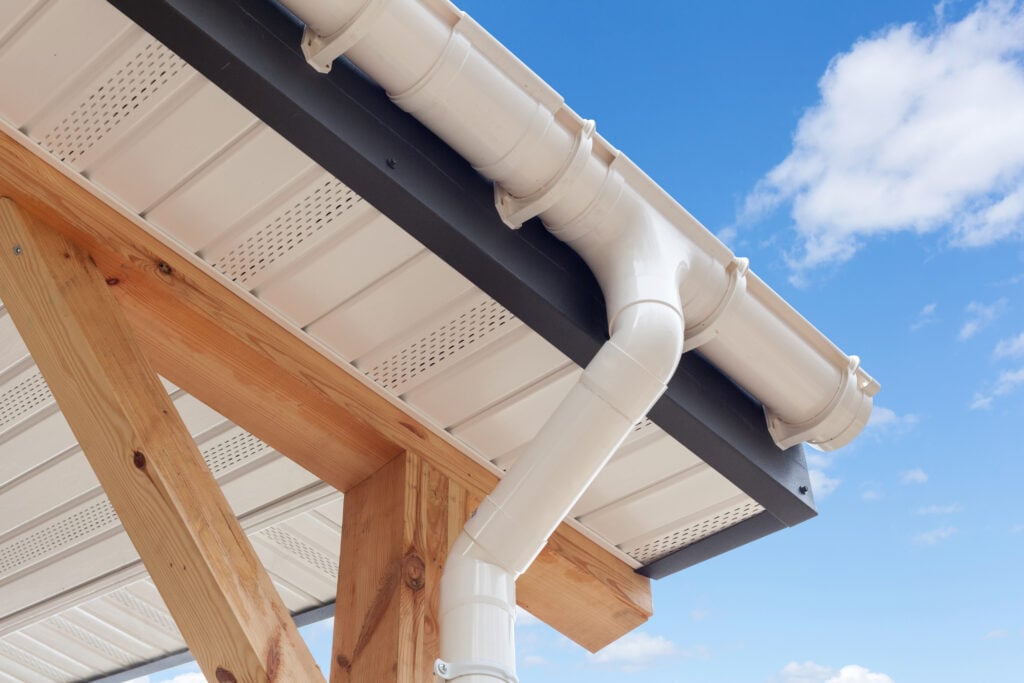 eave vs soffit SIP panel house construction. New white rain gutter. Drainage System with Plastic Siding Soffits and Eaves against blue sky