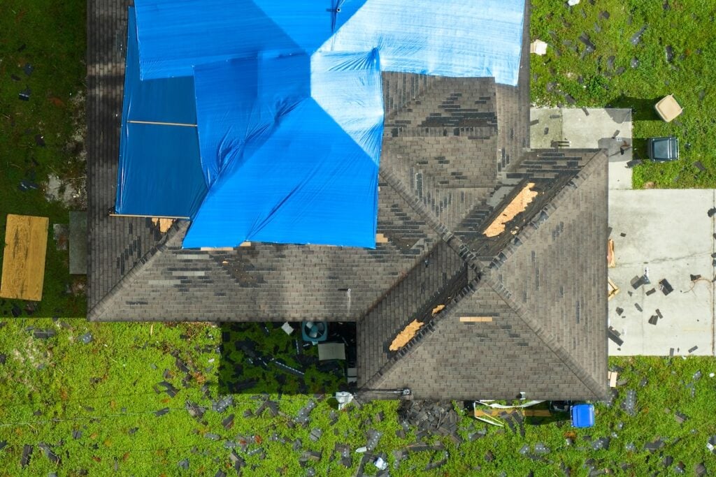 Top view of leaking house roof covered with protective tarp sheets against rain water leaks until replacement of asphalt shingles.